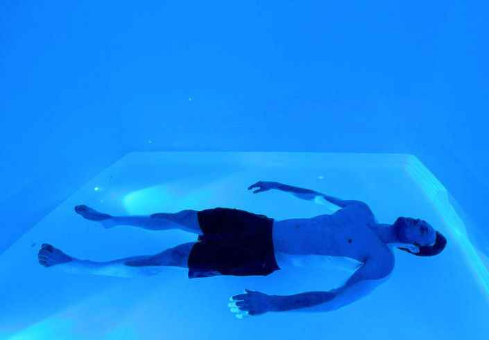 man laying on his back in a blue float tank